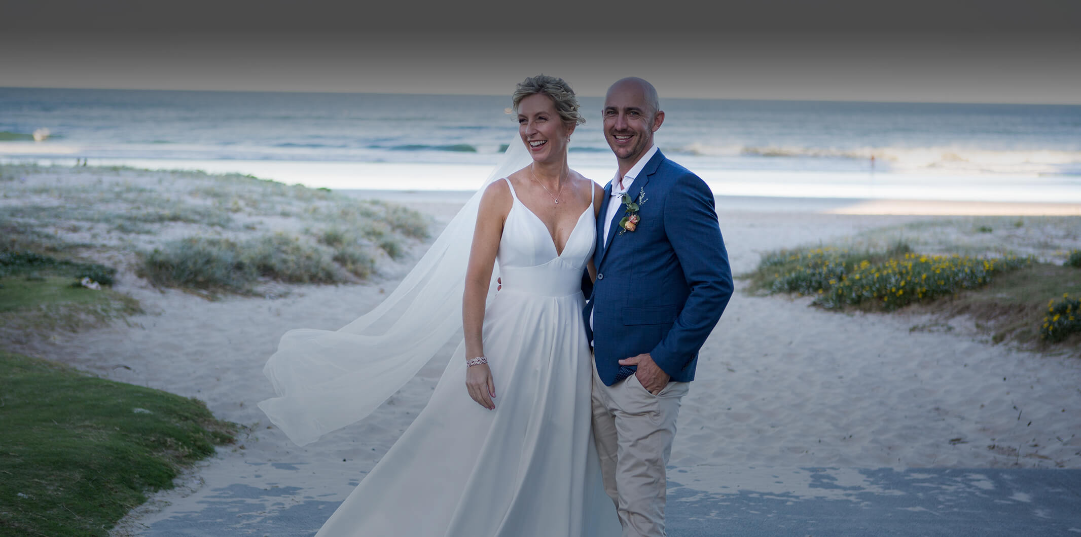 A bride and groom standing in front of the beach
