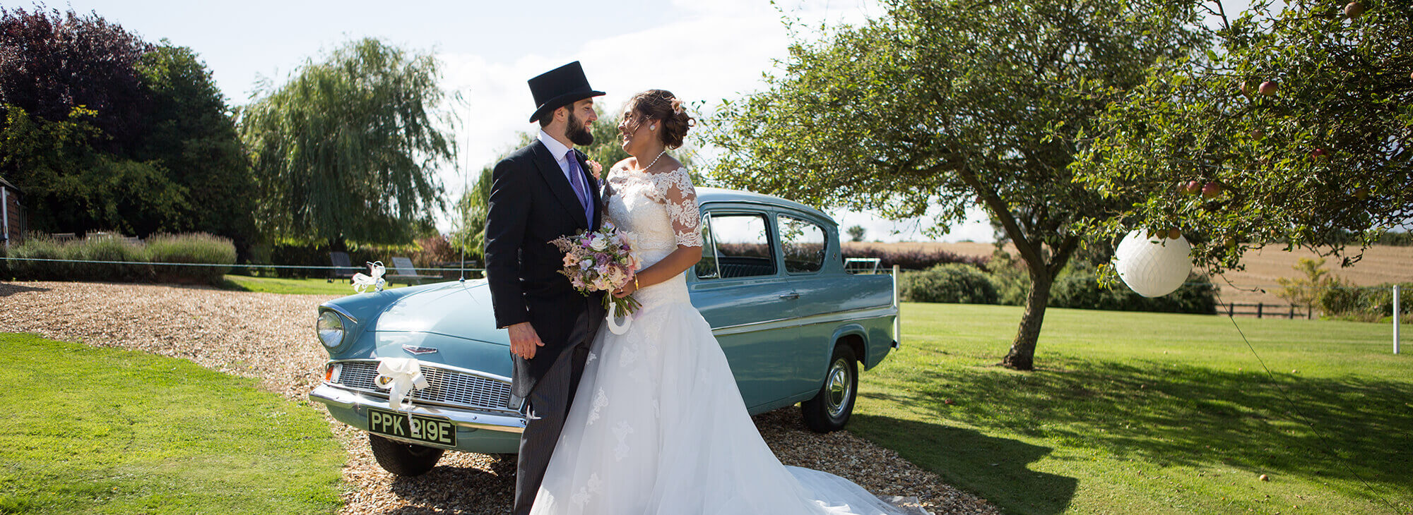 Happy newlyweds smiling in front of vintage car