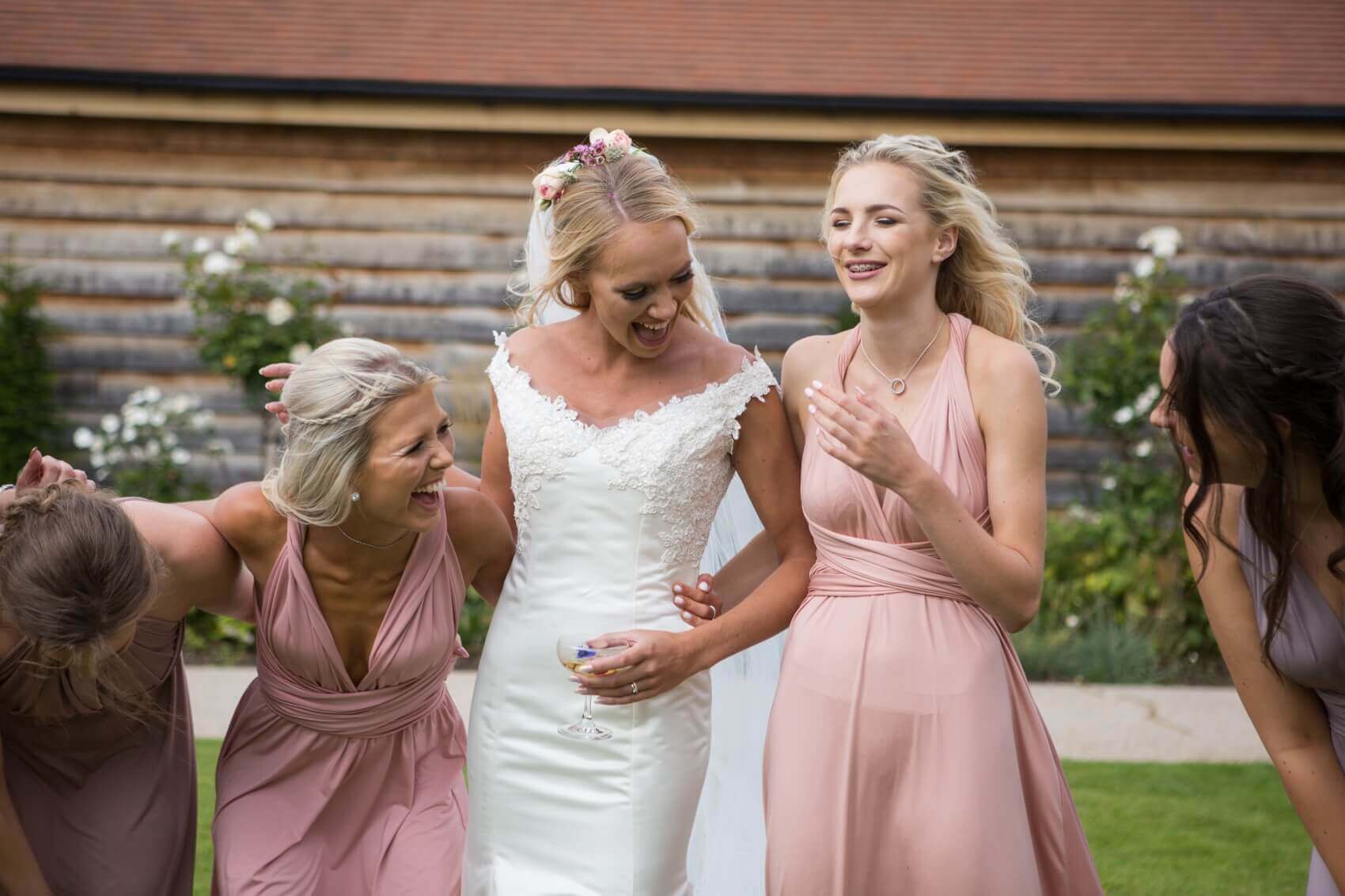 Bride with her bridesmaids laughing in the grounds of Bassmead Manor Farm Barns