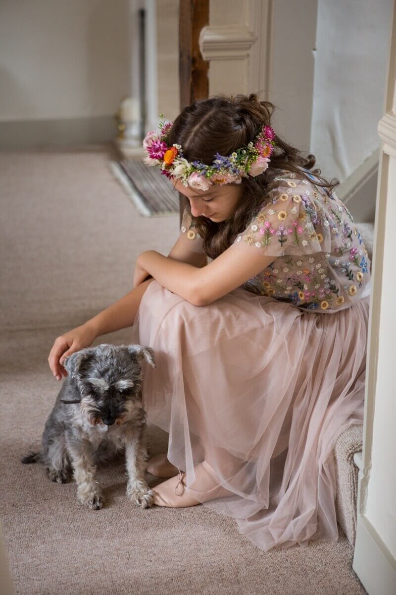 Flower girl in pink with a flower hair crown stroking a dog