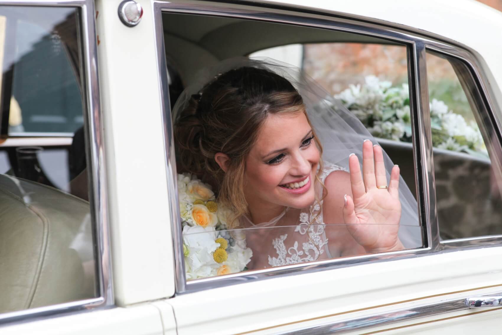 Wedding car with the beautiful bride waving to the guests 