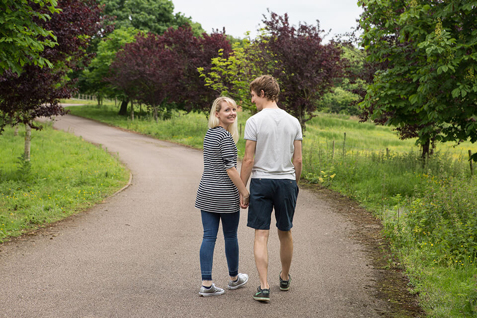 engaged couple walking down a path looking back at the camera