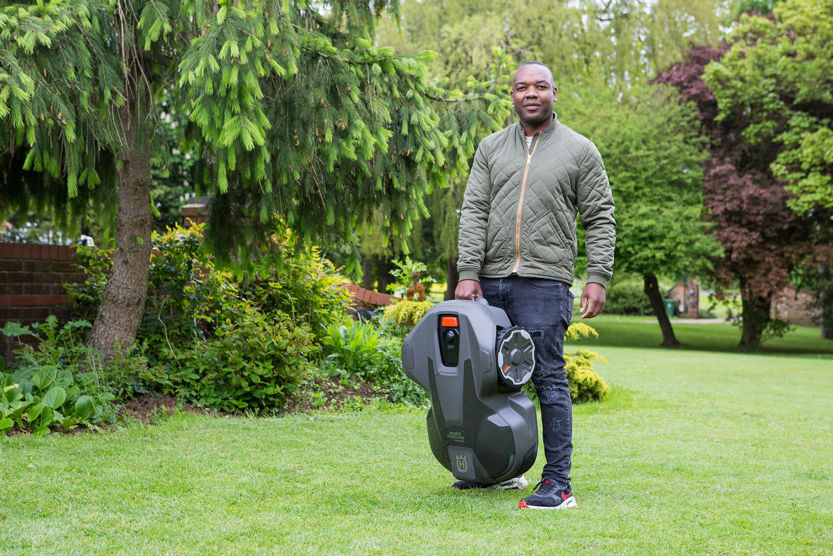 A man smiling holding a lawn mower in a garden