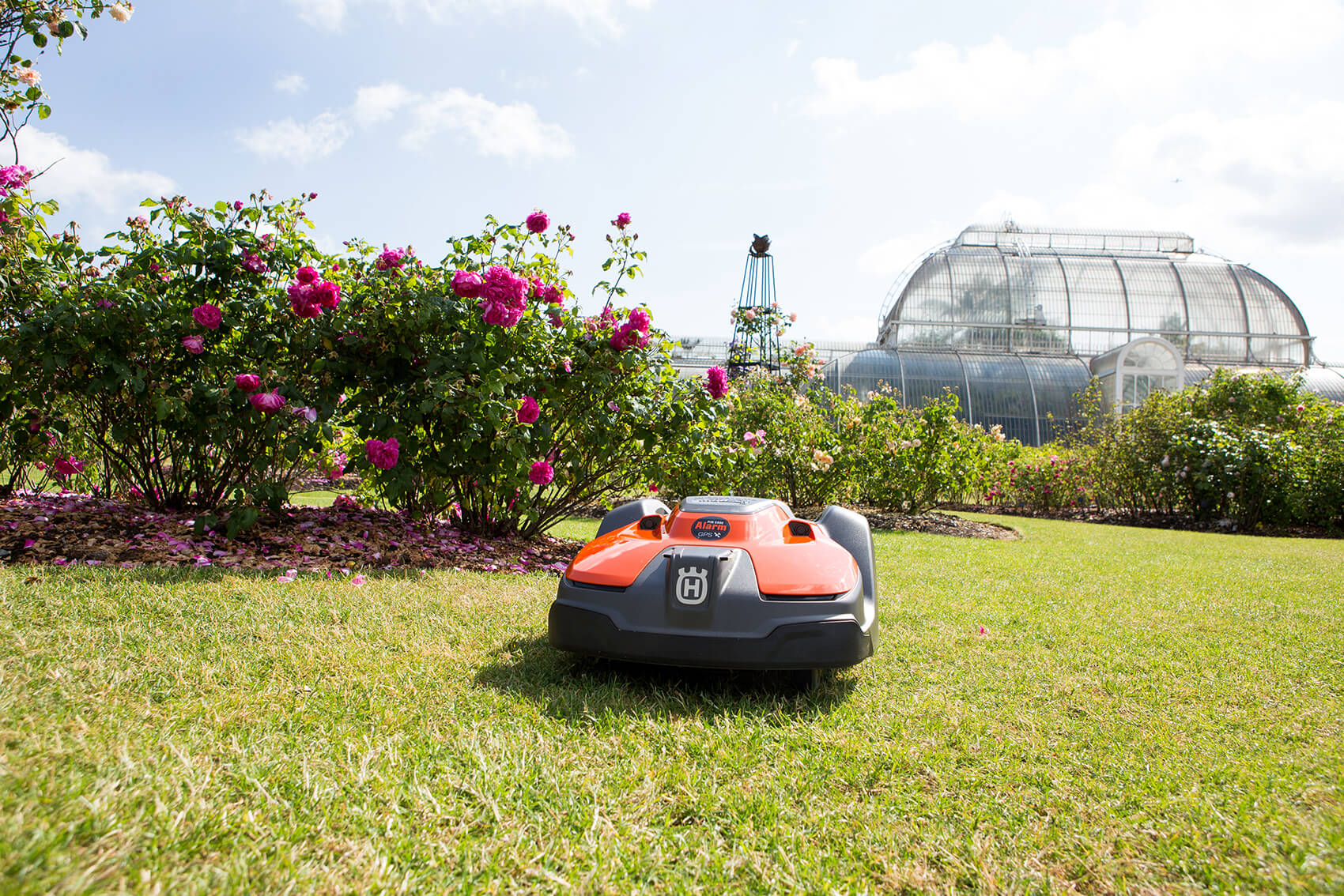 A lawn mower on grass in front of a greenhouse