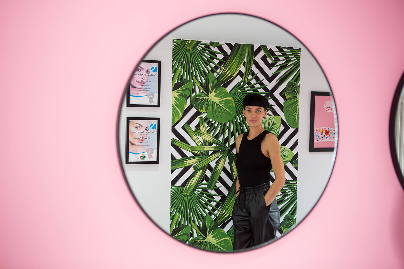 A woman smiling into a mirror on a pink wall