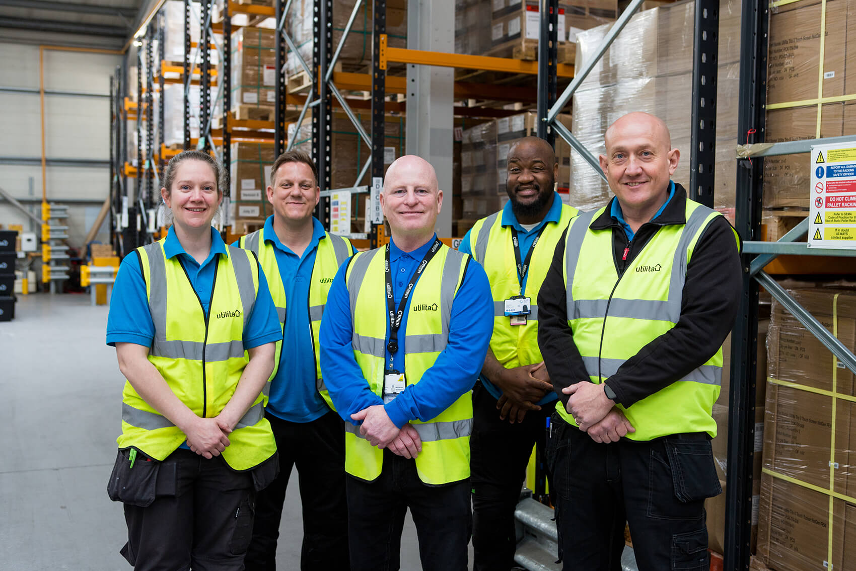 Five people in high-vis jackets smiling in a warehouse