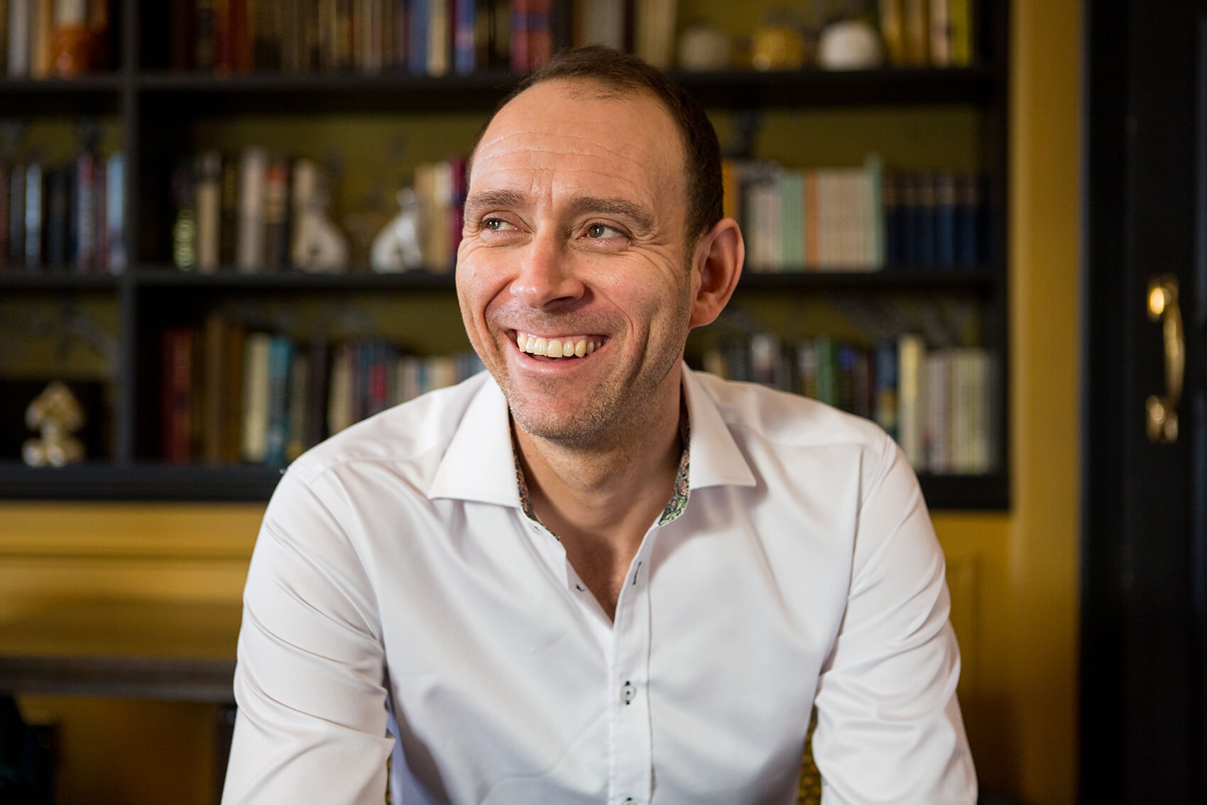 A man smiling with a bookshelf behind him