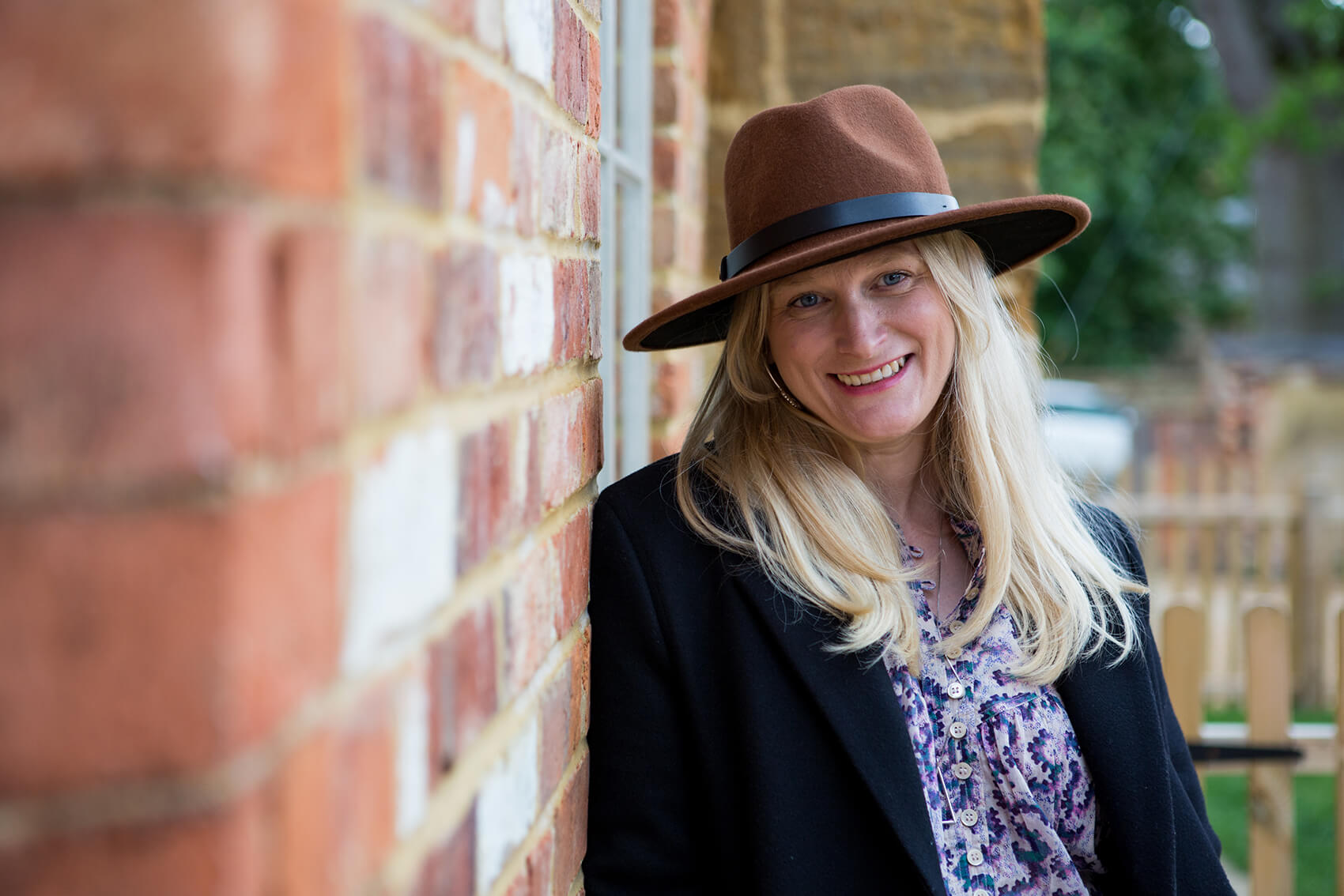 A woman with a hat leaning against a wall