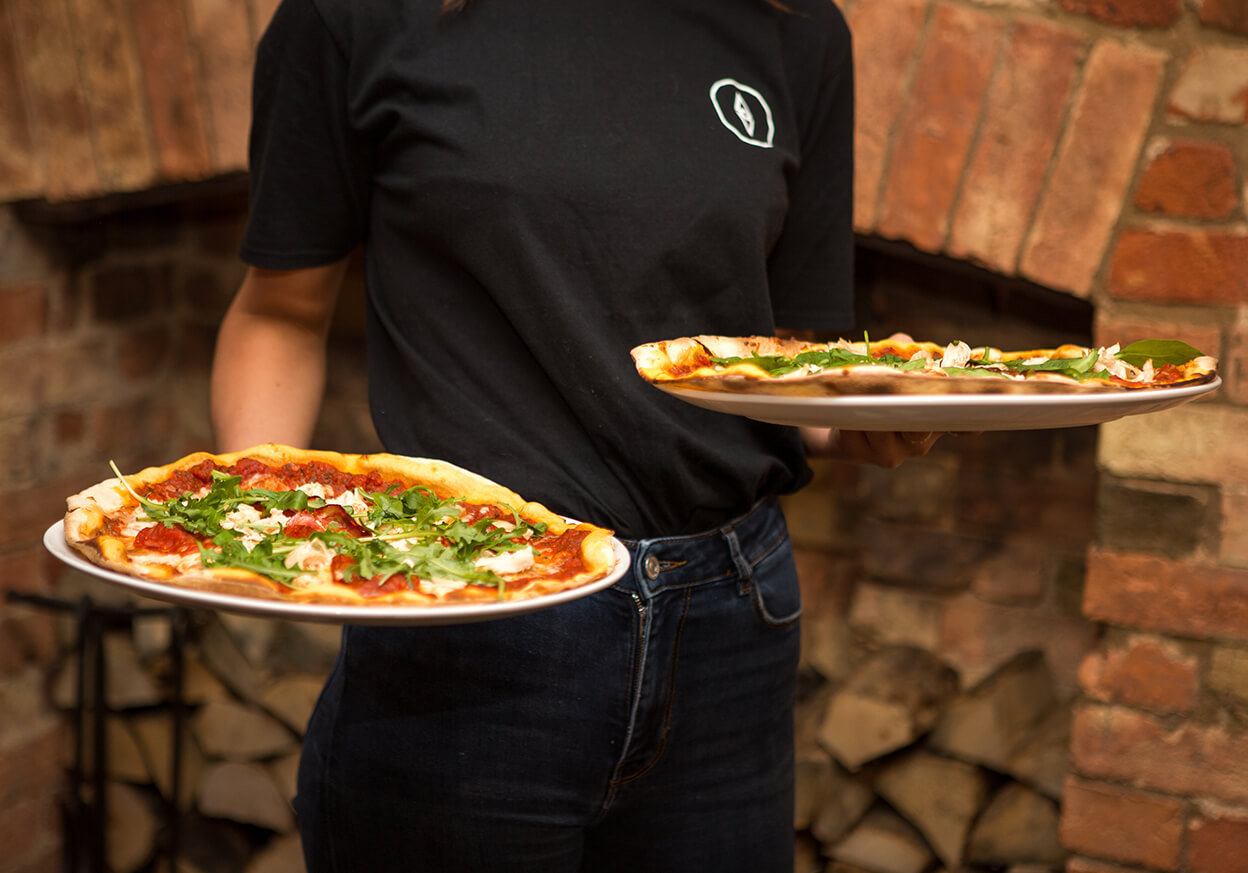 Server holding two freshly cooked pizzas