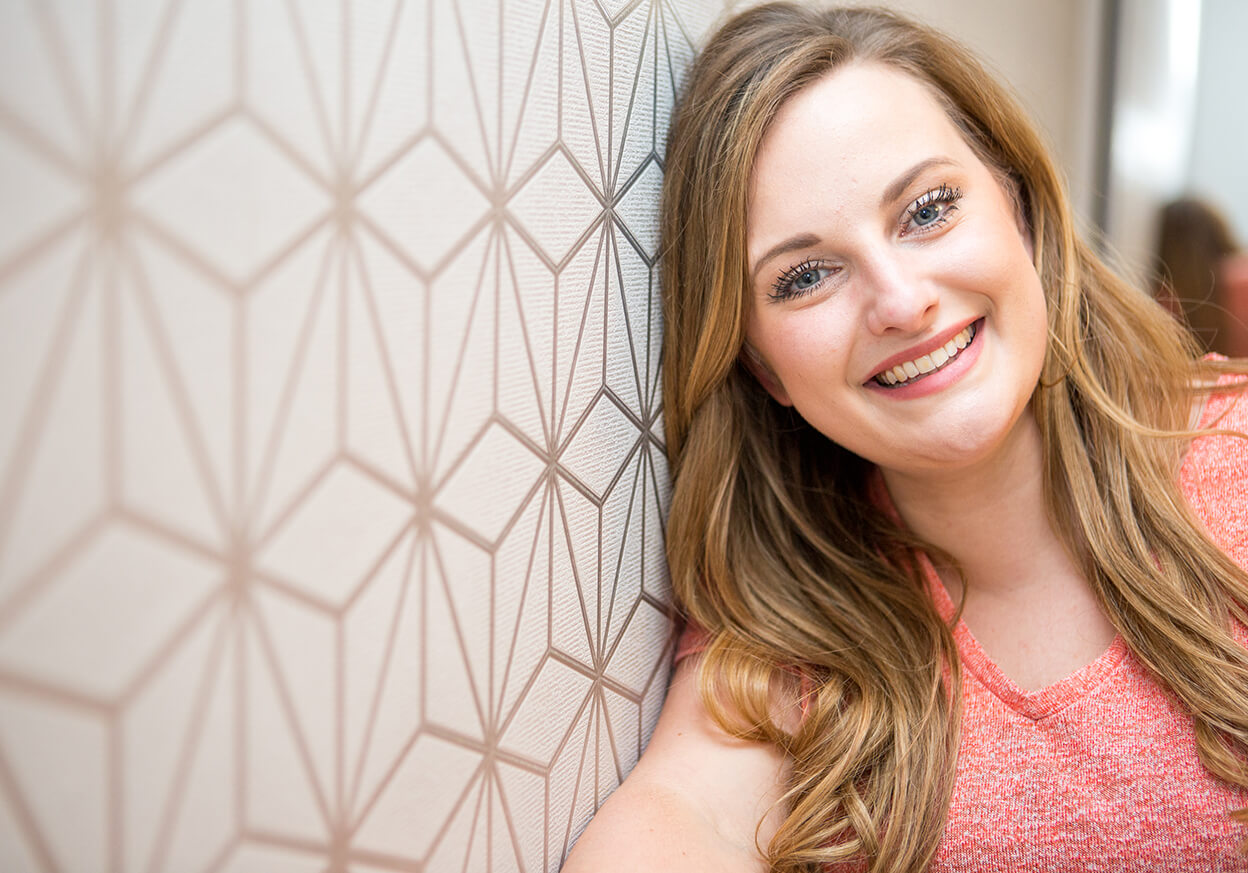 Woman leaning against a wall smiling into a camera