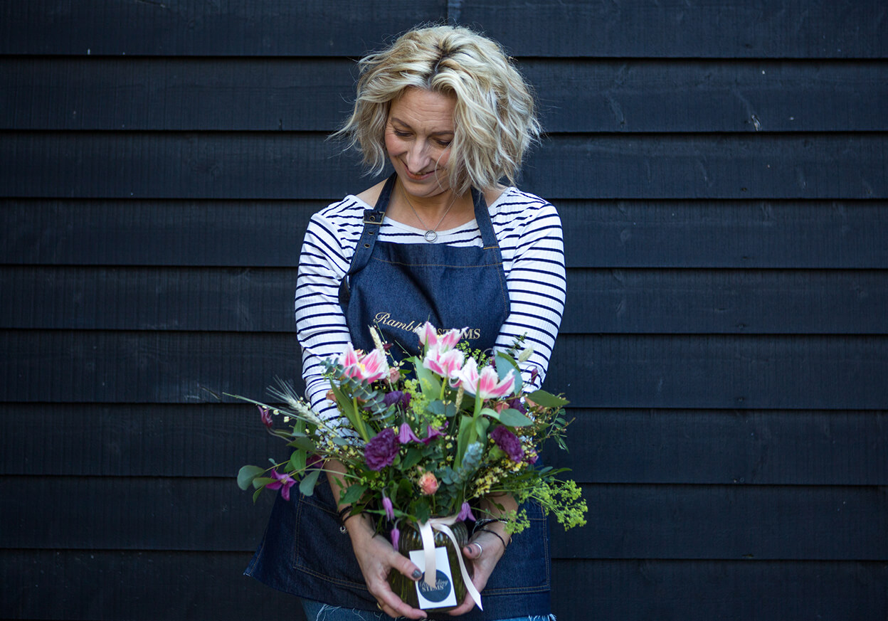 Woman holding a vase of flowers in front of a blue background