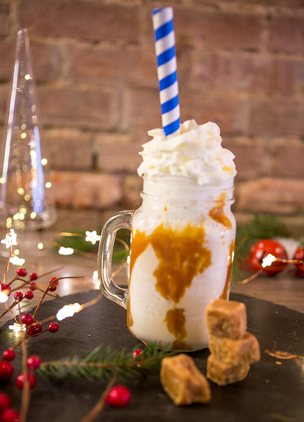 Toffee milkshake in a glass mug with a blue and white striped straw