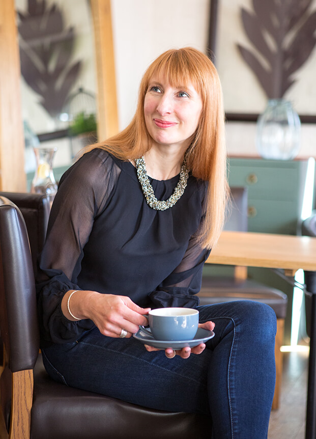 Woman sat smiling while drinking a cup of coffee