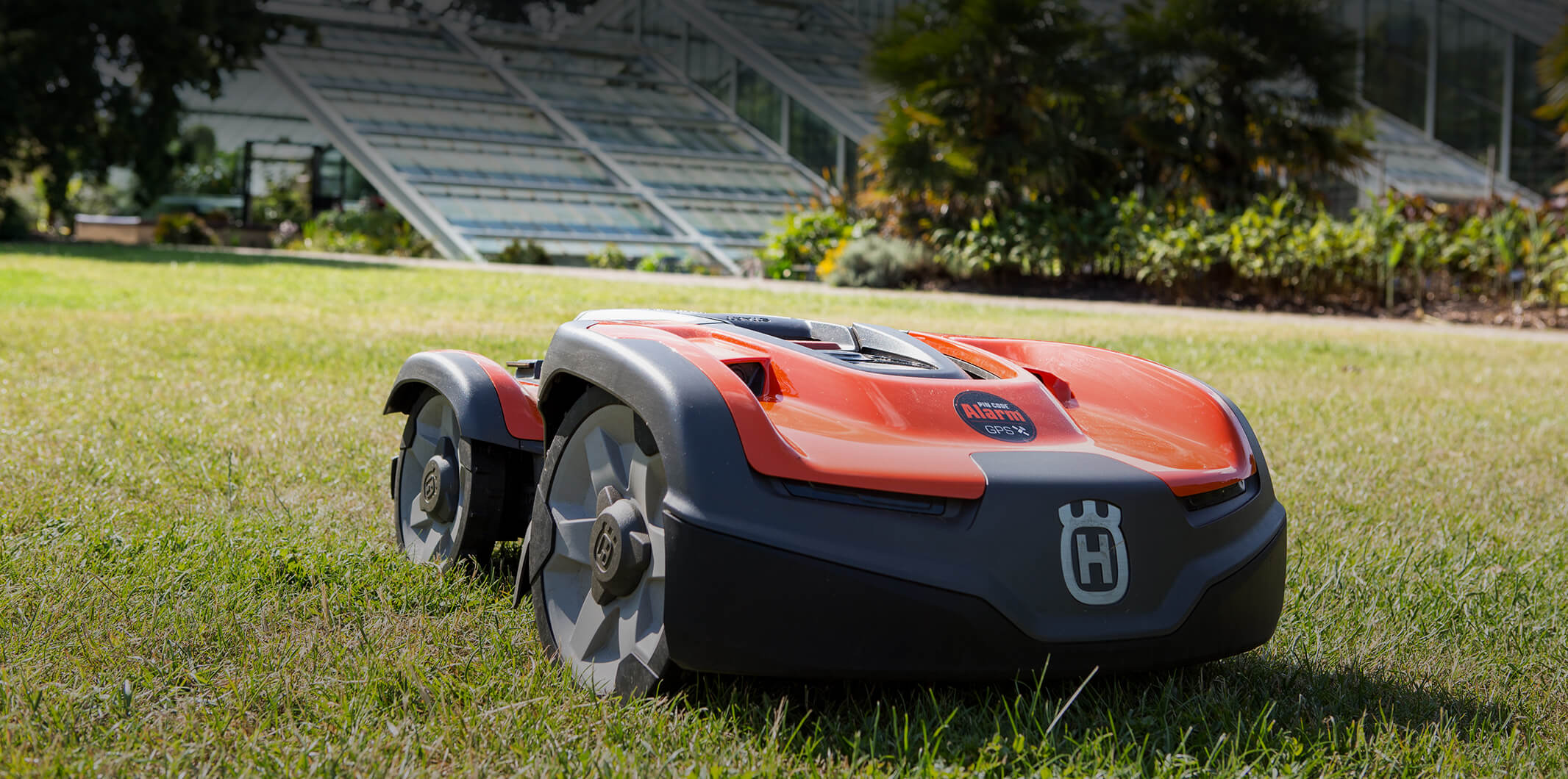 Lawn mower on grass with a glasshouse in the background