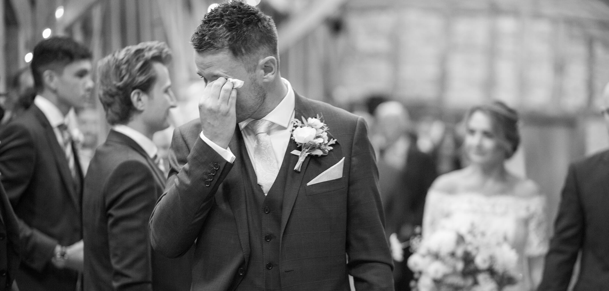 A groom wipes away a tear upon seeing his bride walk down the aisle