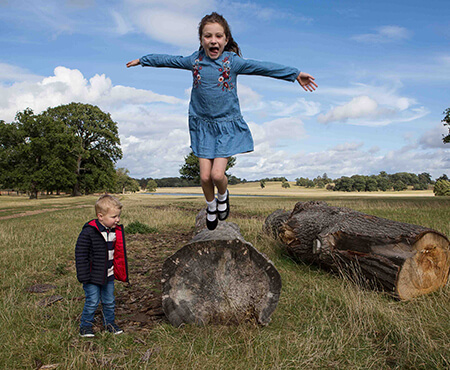 Young girl jumping off wooden tree stump