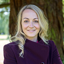 Woman in purple coat standing in front of a tree