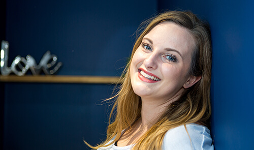 Woman smiling and leaning against a blue wall