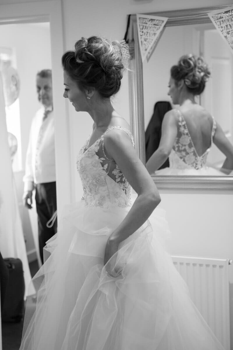 wedding photographer capturing in black and white photo of the bride looking around the door to her father.