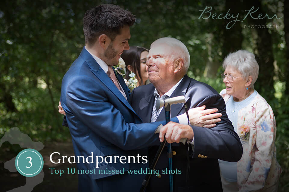 A grandfather and groom embrace at a wedding